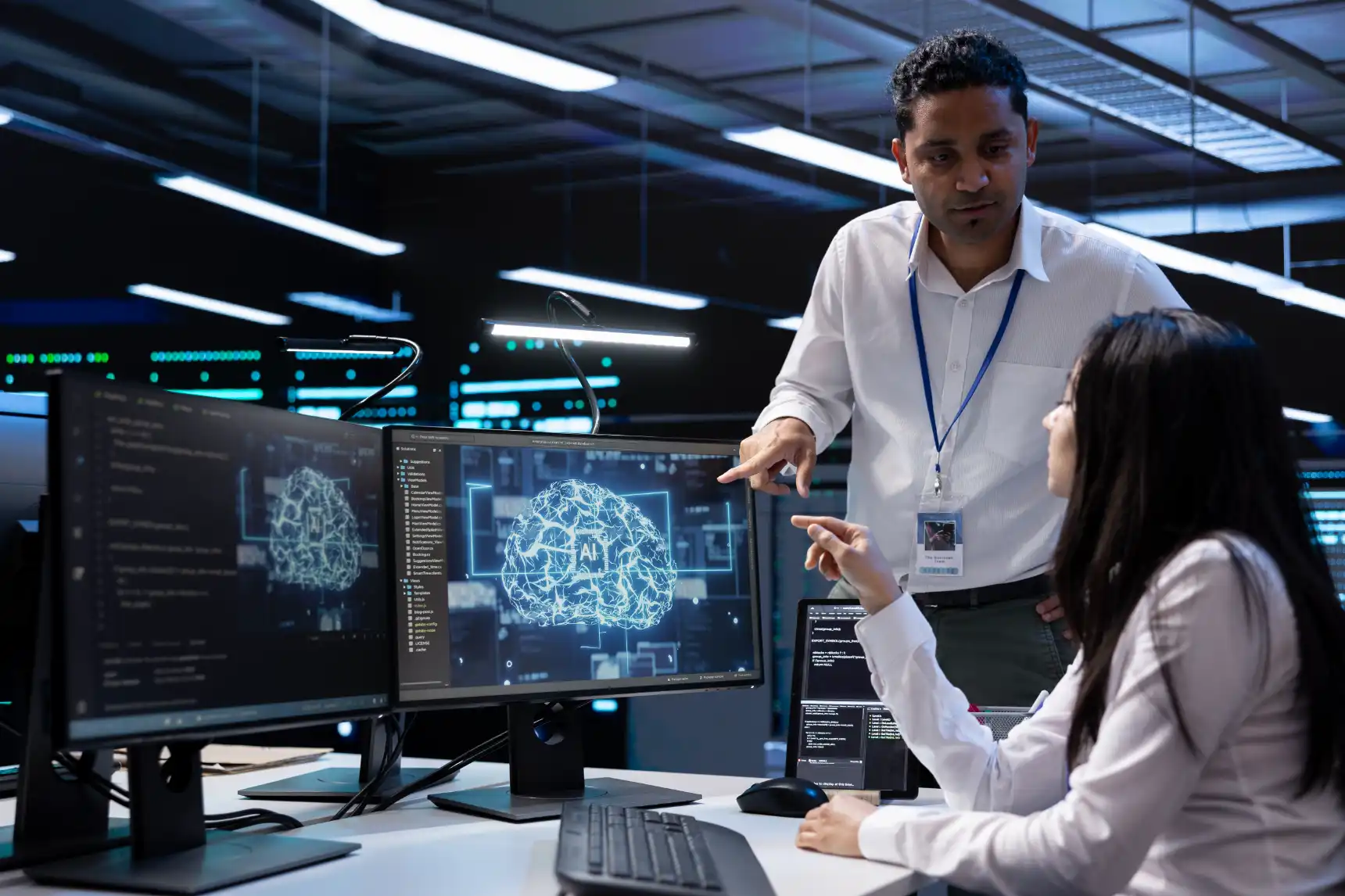 AI developers discussing a digital brain visualization on dual monitors.