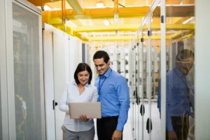 Two data center technicians smiling while reviewing information on a laptop. - SMB Cybersecurity Solutions