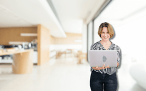 A professional in a striped shirt holds a laptop in a modern office with wooden accents. The setting reflects the efficiency of an outsourced IT support costs guide SMB, helping small businesses manage tech expenses effectively.